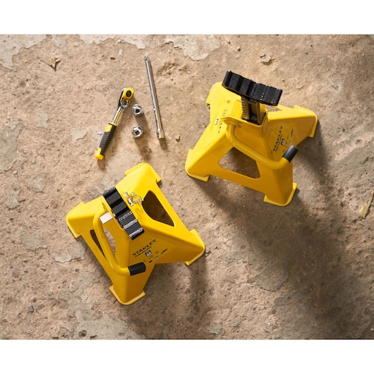 STANLEY STMT81255-1 yellow jack stands and ratchet tool set on rough concrete, top view.