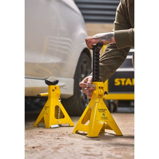 STANLEY STMT81255-1 yellow automotive jack stands in use near vehicle, outdoor setting.