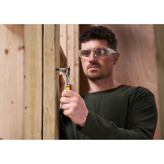 Photo of STANLEY STMT82672-0 ratchet used to fasten screw on wooden frame, close-up of tool in hand.