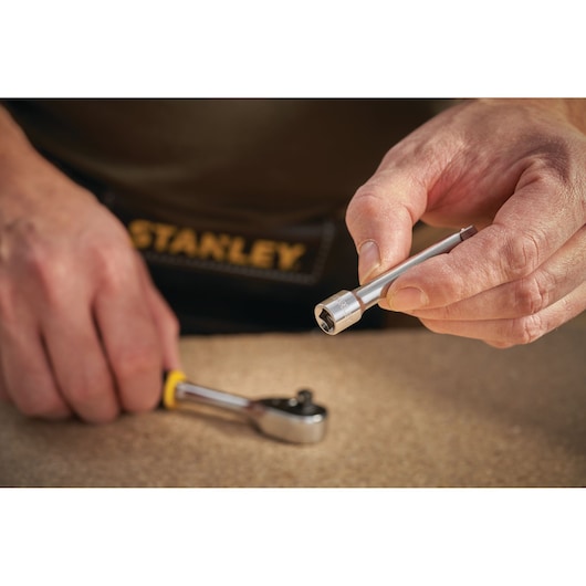STANLEY STMT86006-0 socket extension bar held by hand, ratchet in background, close-up photo.