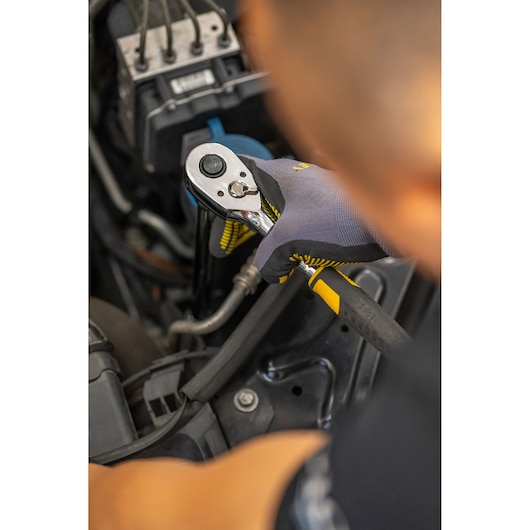 Photo of STANLEY STMT86006-0 ratchet used on car engine by gloved hand, tool visible close-up.