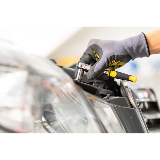 STANLEY STMT86114-0 ratchet wrench in use on car headlight, close-up photography with gloved hand.