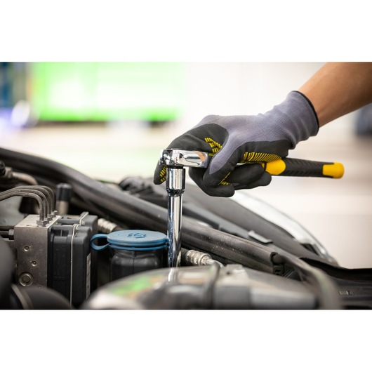 STANLEY STMT86407-0 ratchet wrench in use by gloved hand tightening bolt on car engine, side angle.