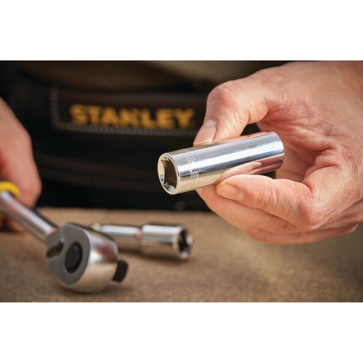 Photo of STANLEY STMT88994-0 chrome socket tool held by hand, with ratchet and extension on table.