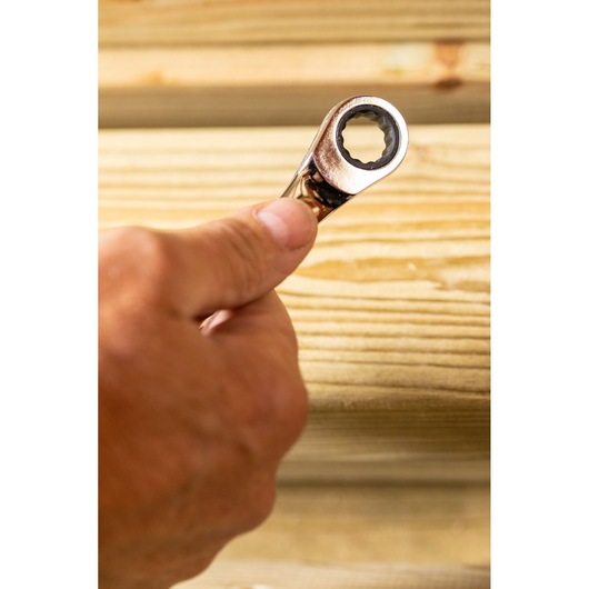 STANLEY STMT89916-0 ratcheting wrench held in hand, close-up, against light wood background.
