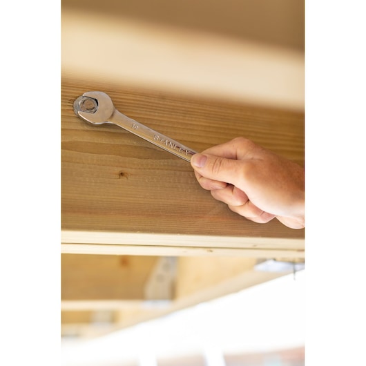 STANLEY STMT95789-0 wrench in use on a bolt against wooden beam, photography close-up.