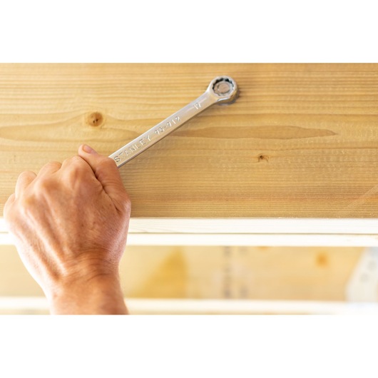 STANLEY STMT95793-0 ratcheting wrench used on a bolt under wood, hand gripping tool.