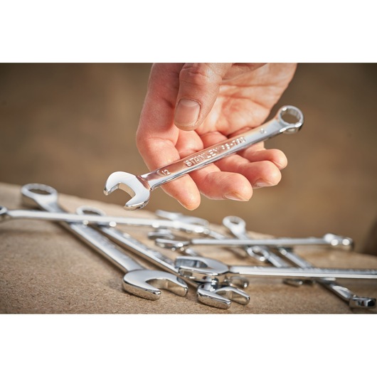Photo of STANLEY STMT95912-0 chrome combination wrench held in hand with other wrenches on table.