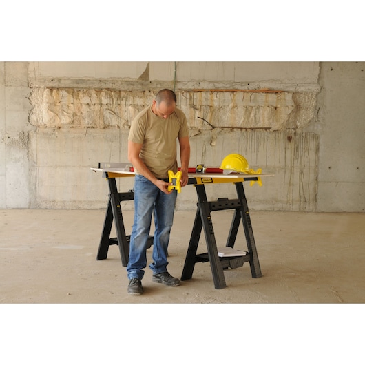 STANLEY STST1-70559 photography of folding sawhorse used for construction with tools and safety helmet.