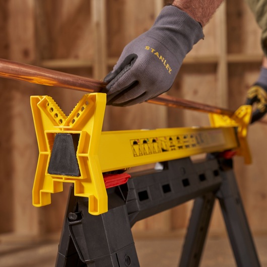 STANLEY STST1-70559 photography of yellow plastic saw horse holding copper pipe in workshop.