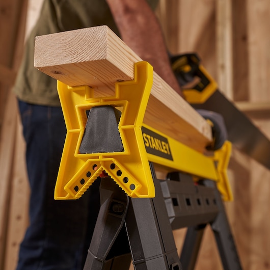 STANLEY STST1-70559 saw horse holding a wooden plank, close-up side angle, in a workshop setting.