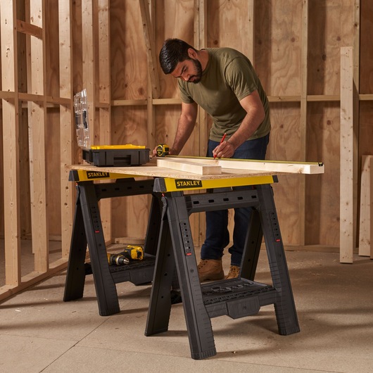 Stanley STST1-70559 plastic sawhorse pair with yellow tops supporting a work surface in a construction setting.