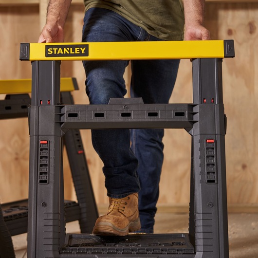 Photo of STANLEY STST1-70559 black and yellow sawhorse in use on a workshop floor.