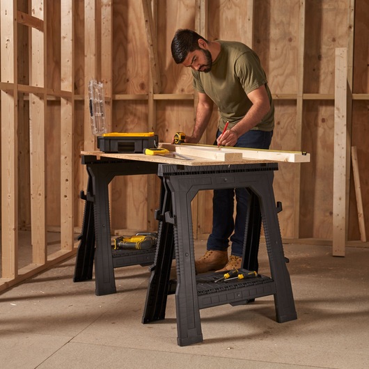 STANLEY STST1-70713 black plastic sawhorses supporting wooden board and tools in construction setting.