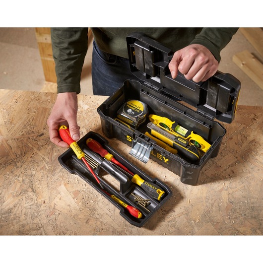 STANLEY STST1-75515 toolbox open on workbench, showing hand tools, level, tape measure, and screws, angled top view.