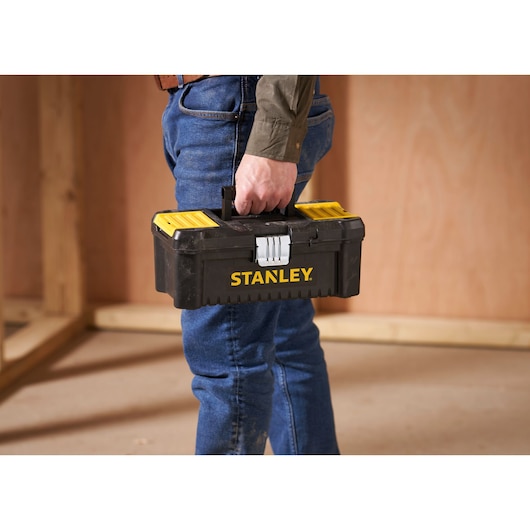 STANLEY STST1-75515 black and yellow toolbox held by person in work site, side view.