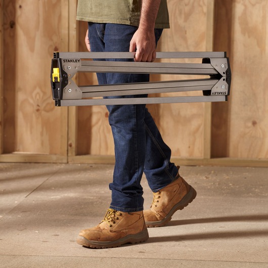Photo of STANLEY STST81337-1 folding sawhorse being carried by a person in work boots on a construction site.