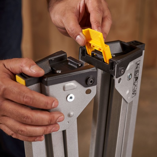 Photo of hands assembling STANLEY STST81337-1 sawhorse leg with yellow locking mechanism.