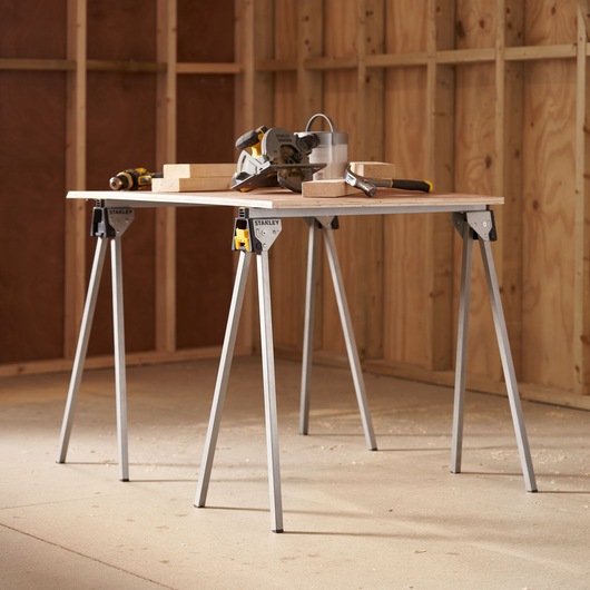 STANLEY STST81337-1 folding sawhorse table in workshop with tools and wood blocks on top.