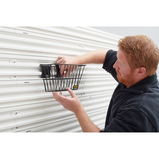 STANLEY STST82603-1 wire basket mounted on white slat wall, person placing items inside.