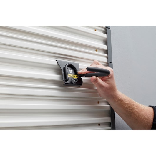 STANLEY STST82616-1 wall-mounted metal hook being used on a corrugated white panel, close-up view.