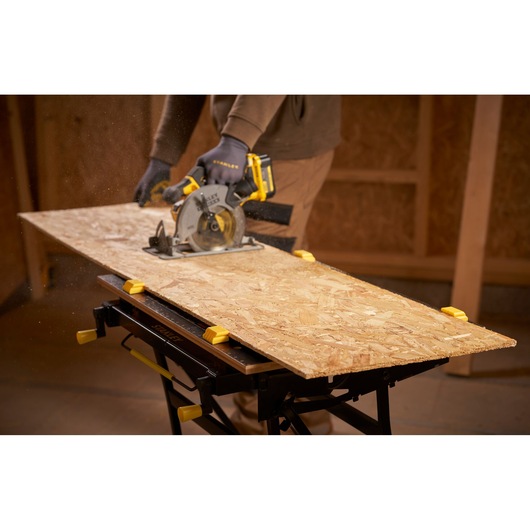 STANLEY STST83800-1 workbench in use, holding plywood with yellow clamps during sawing in a workshop.