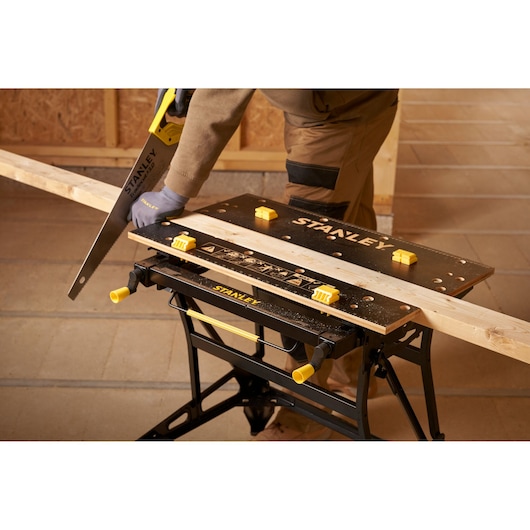 Stanley STST83800-1 workbench with wood plank, handsaw, and person sawing in workshop. Photography product.
