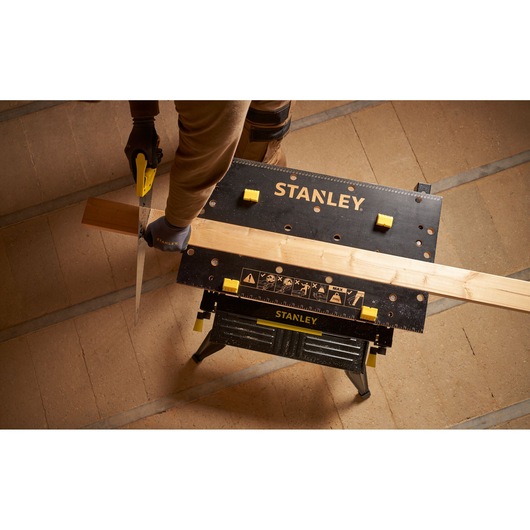 STANLEY STST83800-1 workbench in use, holding wood for sawing, photographed from above on workshop floor.