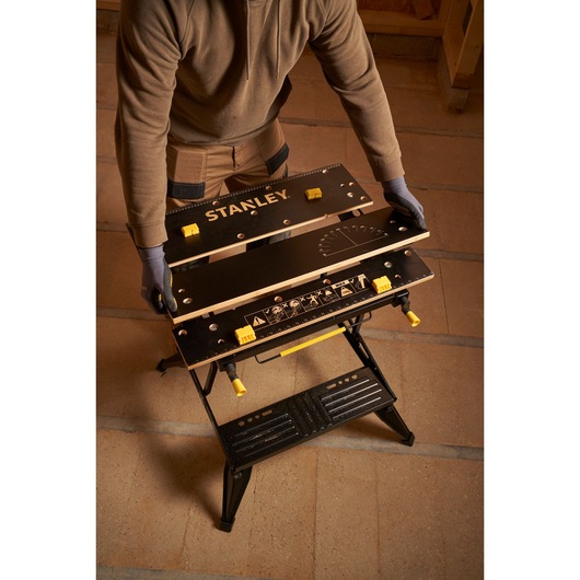 STANLEY STST83800-1 workbench with black tabletop and yellow adjustment knobs, angled from above.