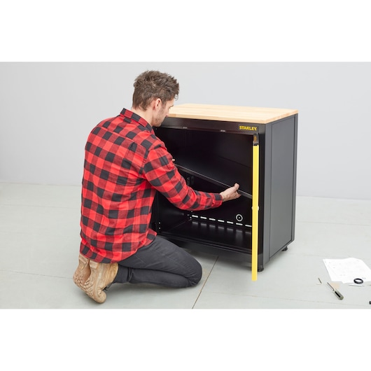 STANLEY STST97595-1 photography of a person assembling a black cabinet with wood top, instructions nearby.