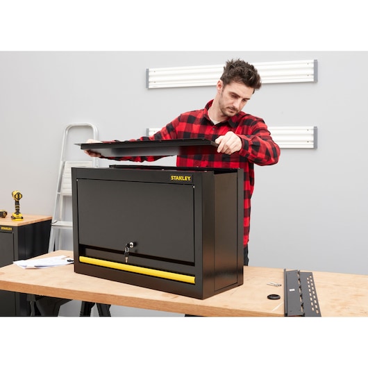 STANLEY STST97599-1 black steel tool cabinet with yellow handle, person assembling on workbench.