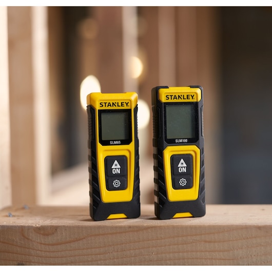 STANLEY FMHT77165-0 digital laser distance meters SLM65 and SLM100 on wooden surface, front view.