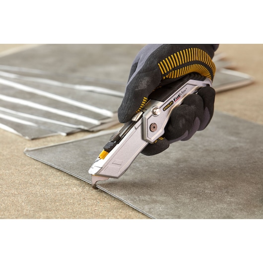 STANLEY XTHT0-10502 utility knife cutting tile, close-up photo, worker wearing black glove.