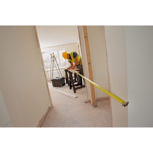 STANLEY XTHT0-33501 tape measure used by worker in construction site, yellow color, extended across doorway.