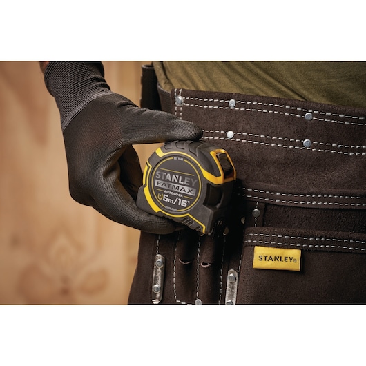 STANLEY XTHT0-33503 tape measure FATMAX 5m, held by gloved hand, tool belt close-up.