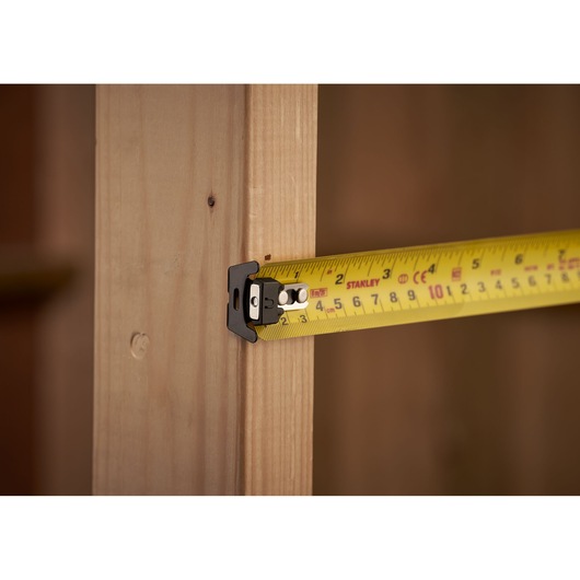 Photo of STANLEY XTHT0-33504 tape measure extended against wooden frame, close-up angle.
