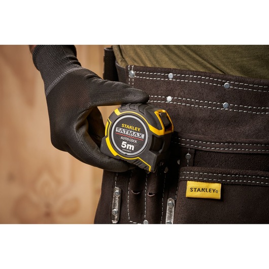 STANLEY XTHT0-33671 tape measure held by gloved hand, shown clipped to tool belt, close-up view.