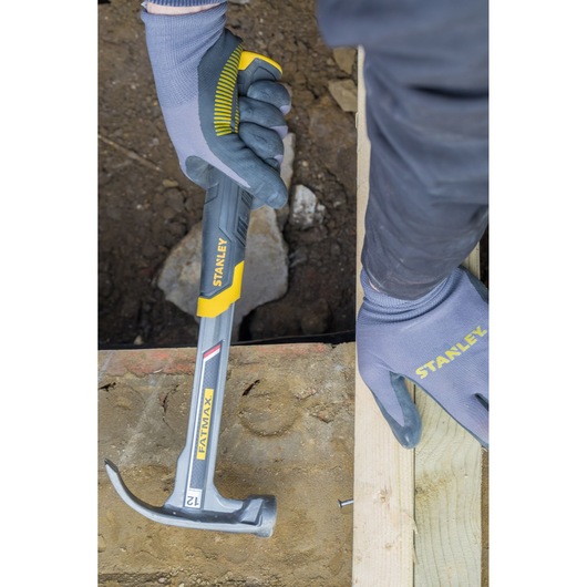 STANLEY XTHT1-51148 claw hammer in use, silver with yellow handle, shown nailing wood, person wearing gloves.